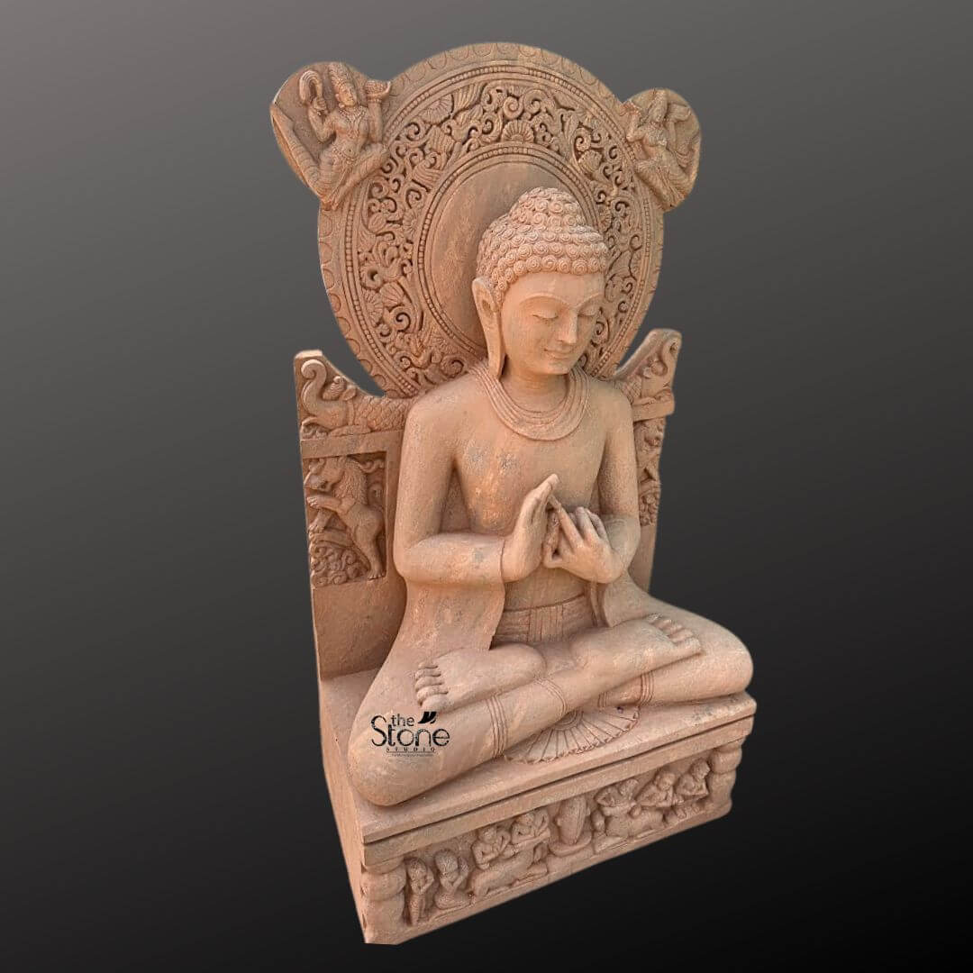 Sandstone Buddha Statue in Dharmachakra Mudra 5ft 4 A full-body studio photograph of a magnificent 5-foot tall Teaching Buddha Sandstone Statue presented in a three-quarter profile against a neutral dark gray gradient background. The statue is masterfully carved from a warm reddish-brown sandstone exhibiting a rich natural texture. The Buddha is seated in the traditional lotus position on a rectangular pedestal with both legs crossed and soles of the feet visible conveying a sense of profound tranquility and meditative grace. His hands are held at chest level in the Dharmachakra Mudra the gesture of teaching and turning the wheel of Dharma with the thumb and index finger of both hands touching to form circles. The figure of the Buddha displays exquisite detail with a serene compassionate expression downcast eyes, and a gentle smile. His hair is arranged in tight traditional curls leading up to the ushnisha and he has elongated earlobes. He is draped in simple finely-pleated robes that fall naturally over his body showcasing the high level of artistry involved in this handcrafted piece. The smooth yet tactile surface of the sandstone emphasizes the sculptural form and the care taken in its creation, making it a stunning example of traditional stone carving. Behind the seated Buddha rises a highly ornate intricately carved prabhamandala or halo. This circular aureole is adorned with elaborate relief patterns including stylized floral motifs celestial figures and mythical creatures adding to the statue's divine aura. The seat itself features carvings of elephants further enhancing the grandeur of the sculpture. The statue rests upon a robust pedestal which is also decorated with carved panels depicting rows of devotees and other figures in reverent postures. The overall composition highlights the monumental scale and spiritual presence of this significant Teaching Buddha Sandstone Statue.