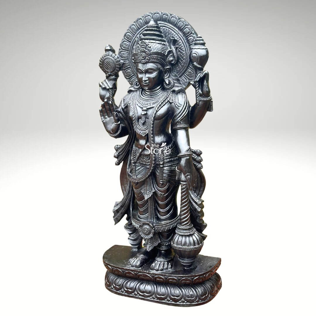Black Stone Narayana Swamy Statue 3.5ft 13 A 41-inch Narayan Swamy blackstone statue is shown in a clean product-style image standing gracefully on a carved pedestal with a traditional temple idol appearance. The deity is depicted in an upright posture with four arms holding sacred symbols associated with Lord Vishnu including the chakra and shankha while one hand is raised in a blessing gesture. The statue features a serene facial expression an ornate crown elongated earrings layered necklaces armlets waist ornaments and finely carved garments that reflect the devotional beauty of a Temple Narayana Swamy Idol. The blackstone finish gives the Narayan Swamy statue a rich, polished and timeless look while the detailed carving highlights the craftsmanship across the body jewellery weapons and decorative halo behind the head. A circular prabhavali frames the upper portion of the idol adding a divine and temple-like presence to the sculpture. The pedestal is decorated with lotus-style carvings and ornamental borders giving the statue a strong and graceful foundation suitable for sacred placement. This image connects perfectly to an article about a Temple Narayana Swamy Idol by showing the spiritual elegance traditional iconography and detailed artistry of a 41-inch Narayan Swamy blackstone statue. The idol is suitable for temples pooja rooms home shrines spiritual centres and devotional interiors where a finely crafted Vishnu form is desired. Its polished blackstone appearance sacred symbols blessing posture and intricate temple-style detailing make it a meaningful choice for worship divine décor and traditional Indian spiritual spaces.