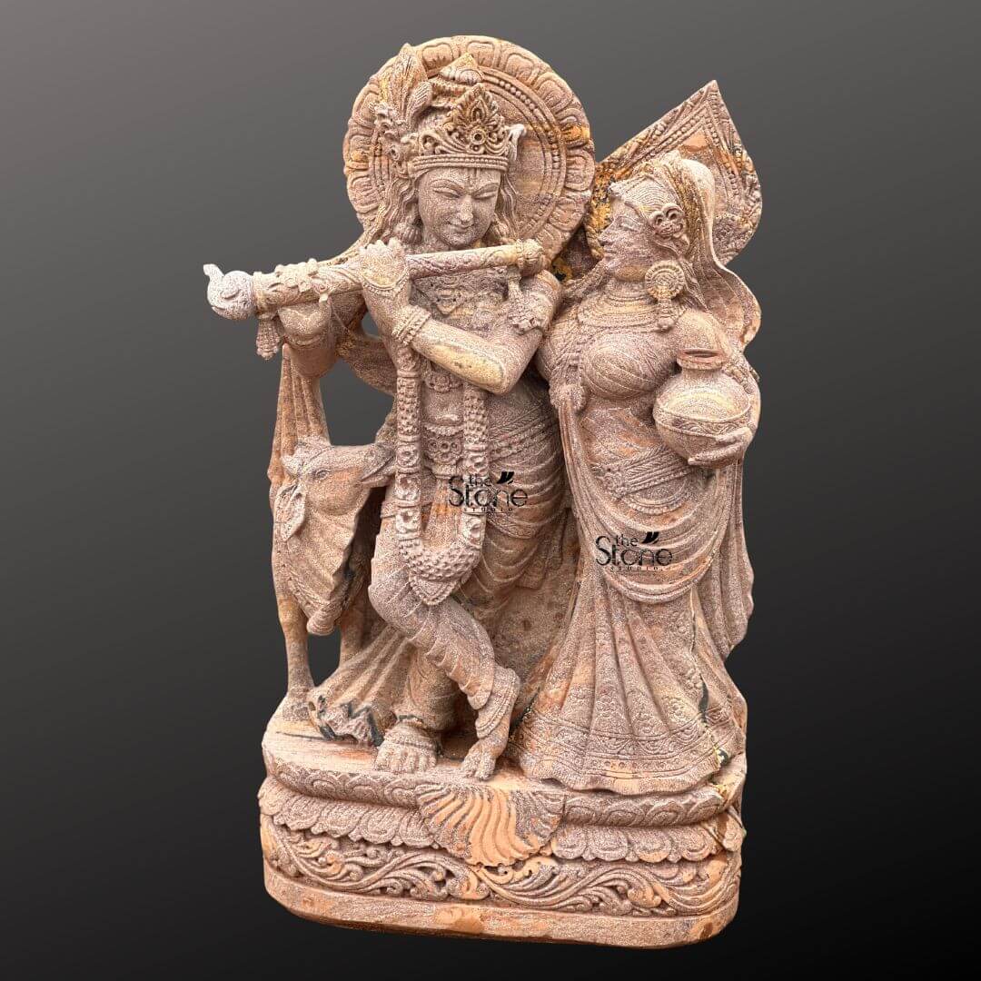 Radha Krishna Stone Statue with Cow 4ft 4 A magnificent 4-foot Traditional Radha Krishna Stone Idol with Cow intricately carved from warm reddish-brown sandstone stands gracefully against a dark gradient background radiating divine love and harmony. The statue depicts Lord Krishna and Radha in a loving traditional standing pose. Krishna distinguished by his elaborate crown and serene expression holds a flute to his lips poised as if playing a melodious tune. Radha stands gracefully beside him adorned with a similar crown and traditional attire her gaze fixed on Krishna while she carries a pot of water or butter symbolizing her devotion and nurturing spirit. This detailed carving beautifully captures their divine romance and pastoral setting in a classic style. The craftsmanship is exquisite with intricate details defining their elaborate crowns delicate jewelry and flowing traditional garments. The sandstone's natural texture and subtle variations in color enhance the antique feel of the sculpture bringing out the tender expressions on their faces and the intricate patterns of their attire. A halo-like circular aureole with ornate patterns frames Krishna's head further emphasizing his divine presence. A key element central to the article's title is the inclusion of a small docile cow depicted near Krishna's feet symbolizing his role as a protector and caretaker of cattle and adding to the pastoral charm and traditional iconography. The entire ensemble rests on a multi-tiered intricately carved pedestal adorned with lotus petal designs and other traditional motifs providing a stable and dignified foundation. The depth and detail of the carving across the entire 4-foot statue are remarkable showcasing the artistry of the piece. This Sandstone Traditional Radha Krishna Stone Idol with its endearing depiction of a cow is an exquisite example of religious artistry designed to bring blessings love and aesthetic beauty to any home or temple making it an ideal focal point for devotion perfectly aligning with an article focusing on such charming and symbolically rich traditional Radha Krishna statues.