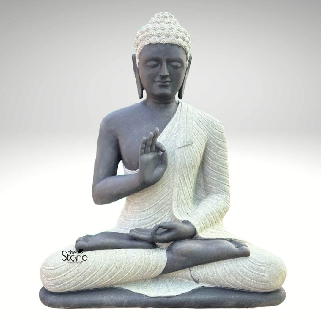 Two Tone Buddha Stone Statue for Home 3ft 1 A serene hand-carved Blackstone Buddha Stone Statue sits in a traditional meditative pose presented in a clean studio setting against a soft grey background. The three-foot-tall statue showcases a striking two-tone finish with the Buddha's body and head carved from a deep dark blackstone exhibiting a smooth polished texture that highlights the rich dark tones. This contrasts beautifully with his monastic robes which are rendered in a contrasting lighter grey or off-white stone featuring a subtle granular texture. This distinct separation emphasizes the form of the robes as they drape over his crossed legs and shoulders adding depth and visual interest to the sacred art. The Buddha is depicted seated with his legs crossed in a full lotus position on a simple integrated dark blackstone base. His hands are gracefully positioned in the vitarka mudra symbolizing discussion and the transmission of teachings with the right hand raised and the thumb and index finger forming a circle while the left hand rests in his lap. His facial expression is calm and contemplative with downcast eyes a gentle smile and tightly curled hair leading to a cranial ushnisha all rendered with precise craftsmanship that honors traditional iconography. The overall composition evokes a sense of peace tranquility and spiritual harmony. This three-foot Blackstone Buddha Stone Statue is an ideal illustration for an article discussing a Two Tone Buddha Stone Statue for Home demonstrating how such a piece can transform an indoor space into a peaceful sanctuary. The unique dual-color and dual-texture stone work makes it a stunning focal point for a living room entryway or dedicated meditation area. The traditional design brings a sense of sacred history and calm to any home interior while the durable blackstone construction ensures it is both a beautiful and a meaningful addition to the home.