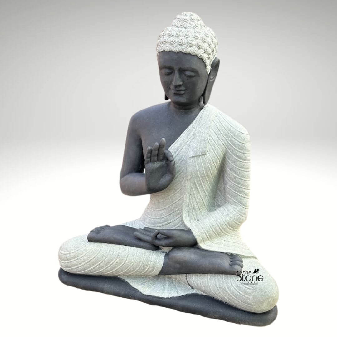Two Tone Buddha Stone Statue for Home 3ft 4 A serene three-foot-tall Blackstone Buddha statue sits in a traditional meditative pose presented in a clean studio setting against a soft grey background. The statue showcases a striking two-tone finish with the Buddha's body and head carved from a deep dark blackstone exhibiting a smooth polished texture that highlights the rich dark tones. This contrasts beautifully with his monastic robes which are rendered in a contrasting lighter grey or off-white stone featuring a subtle granular texture. This distinct separation emphasizes the form of the robes as they drape over his crossed legs and shoulders adding depth and visual interest to the sacred art. The Buddha is depicted seated with his legs crossed in a full lotus position on a simple integrated dark blackstone base. His hands are gracefully positioned in the vitarka mudra symbolizing discussion and the transmission of teachings with the right hand raised and the thumb and index finger forming a circle while the left hand rests in his lap. His facial expression is calm and contemplative with downcast eyes a gentle smile and tightly curled hair leading to a cranial ushnisha all rendered with precise craftsmanship that honors traditional iconography. The overall composition evokes a sense of peace, tranquility and spiritual harmony. This three-foot Blackstone Buddha statue is an ideal illustration for an article discussing a Vitarka Mudra Buddha Statue perfectly demonstrating the specific hand gesture associated with discussion and the exposition of Buddhist philosophy. Its substantial size ensures it functions as a commanding focal point whether placed in a home interior as a spiritual anchor or in a garden setting. The traditional design brings a sense of sacred history and calm to any space while the durable blackstone construction ensures it is both a beautiful and a meaningful addition to its surroundings. The detailed carving and harmonious integration of elements highlight its value as a piece of sacred art.