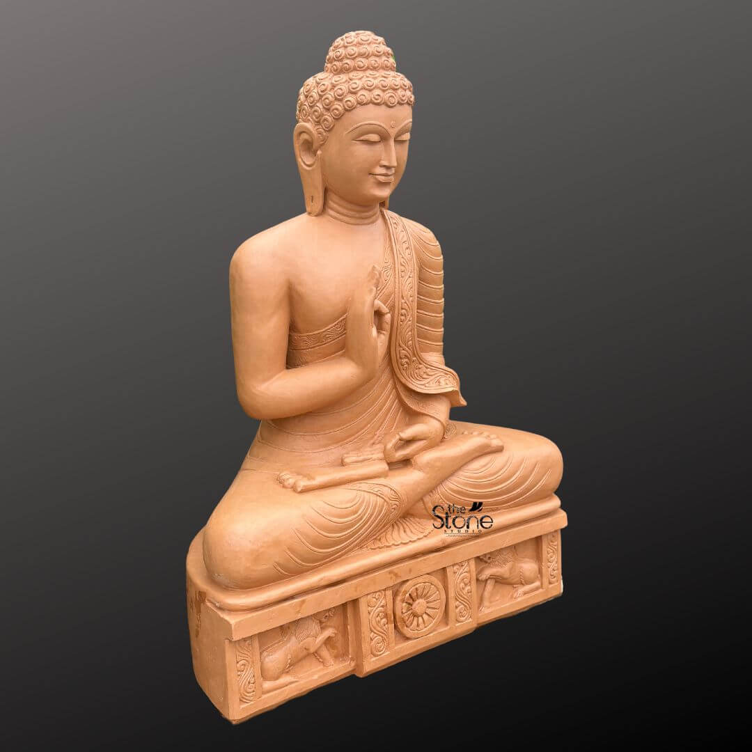 A three-quarter perspective studio photograph presents a magnificent hand-carved 4-foot tall sandstone Buddha statue meticulously crafted for an outdoor garden setting. The statue is carved from warm textured brown sandstone showcasing a natural slightly porous finish that emphasizes its artisanal quality and durability against the elements. It is seated in the traditional vajra lotus position embodying profound peace and meditation. The figure is draped in intricately carved monastic robes with the fabric folds and a decorative patterned border clearly defined on the left shoulder. The Buddha's face is serene with eyes half-closed in contemplation and a gentle smile. The statue sits upon a substantial carved rectangular pedestal that is an integral part of the entire 4-foot structure. This plinth is adorned with detailed bas-relief carvings on its front face. In the center a prominent Dharma Chakra is flanked by sculpted lions ancient symbols of the Buddha's royalty and the spread of his teachings. The entire plinth adds to the statue's monumental presence and cultural authenticity. The sandstone exhibits natural color variations and a tactile weathered look that would harmonize beautifully with natural garden elements like plants, stone pathways and sunlight. This Large Handcrafted Stone Buddha Statue for Garden use is an exceptional piece of art that combines spiritual symbolism with grand scale. The 4-foot height ensures it will be a dominant and inspiring feature in any outdoor space. The warm sandstone material is durable for garden environments and weathers gracefully over time enhancing its ancient and serene appearance. The intricate carvings from the curls of the ushnisha to the figures on the base demonstrate a high level of craftsmanship. The statue's posture and mudra convey a message of tranquility and wisdom making it a perfect addition to create a peaceful sanctuary in a garden. The lighting is even and directional highlighting every detail of the carving against a neutral dark grey background.