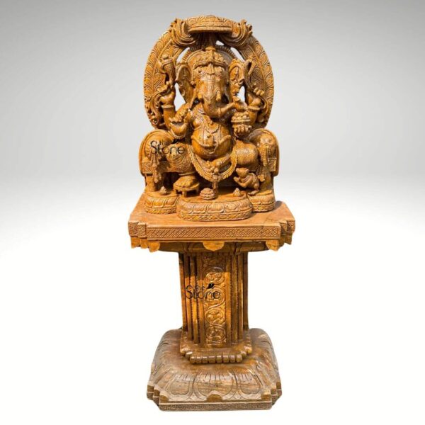 This is a centered full-view photograph of a magnificent hand-carved brown sandstone statue of Lord Ganesha elevated and displayed upon a matching ornate sandstone pedestal. The statue depicts Ganesha in a traditional seated posture known as Vighneshvara on a richly carved throne. He is adorned with intricate traditional jewelry a detailed crown and garlands all carved directly from the warm textured brown sandstone. Ganesha has four arms holding symbolic attributes including an axe a goad and a modak with his primary right hand in the Abhaya mudra of blessing. His form is robust and detailed with a serene facial expression and deeply carved reliefs. The Ganesha statue rests upon a substantial square sandstone pedestal base which is richly carved on all visible sides with traditional motifs including decorative floral patterns and miniature figural reliefs that echo the art style of the main sculpture. The pedestal provides a stable and elegant foundation raising the deity to a prominent height suitable for worship or prominent display as a decor piece. The entire ensemble—statue throne and pedestal—is crafted from the same consistent brown sandstone featuring a beautiful uniform natural grain and a finely textured matte finish that emphasizes the artisan's skill in creating deep complex carvings. The statue and pedestal are presented against a clean seamless light-grey studio background that fades to white isolating the object and allowing its form color and intricate details to be the sole focus. The lighting is soft even and directional illuminating the scene from the front and slightly to the side to cast gentle shadows that define the three-dimensional quality and deep reliefs of the sandstone carving. The overall composition conveys a sense of spiritual reverence traditional artistry and substantial craftsmanship inherent to this type of Indian stone sculpture.