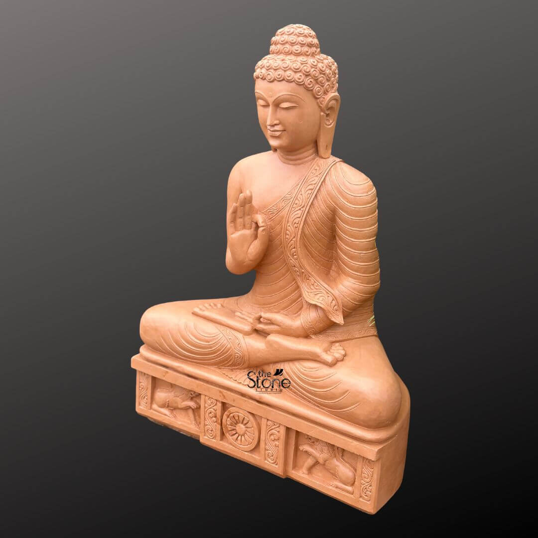 A three-quarter perspective photograph presents a magnificent 4-foot tall Sandstone Gautam Buddha Statue meticulously hand-carved and designed as an imposing spiritual focal point for a home interior. The statue is carved from warm light-brown sandstone showcasing a natural slightly textured finish that emphasizes its artisanal quality and tactile nature. It is seated in the traditional vajra lotus position embodying a profound sense of peace meditation and enlightenment. The Buddha is draped in intricately carved monastic robes with the fabric folds and a decorative patterned border clearly defined on the left shoulder. The figure's face is serene with eyes half-closed in contemplation and a gentle compassionate smile. The statue sits upon a substantial carved rectangular pedestal that is an integral part of the entire 4-foot structure. This plinth is adorned with detailed bas-relief carvings on its front face. In the center a prominent Dharma Chakra is flanked by sculpted lions ancient symbols of the Buddha's royalty and the spread of his teachings. The entire plinth adds to the statue's monumental presence and cultural authenticity within a home setting. The hands are held in the Vitarka Mudra with the right hand raised and the thumb and index finger forming a circle symbolizing the transmission of teachings and intellectual discussion while the left hand rests in the lap in the gesture of meditation. This 4-foot Sandstone Gautam Buddha Statue is an exceptional piece of art that brings spiritual depth and cultural elegance to a home. The substantial height ensures it will be an inspiring and dominant feature in a living room meditation space or grand foyer. The warm sandstone material is durable and has a timeless appeal that complements various home decor styles from traditional to contemporary. The intricate carvings from the curls of the ushnisha to the figures on the base demonstrate a high level of craftsmanship making it not just a religious icon but a valuable art piece. The statue's posture and mudra convey a message of tranquility and wisdom creating a peaceful sanctuary within the home. The lighting is even and directional highlighting every detail of the carving against a neutral dark grey background.