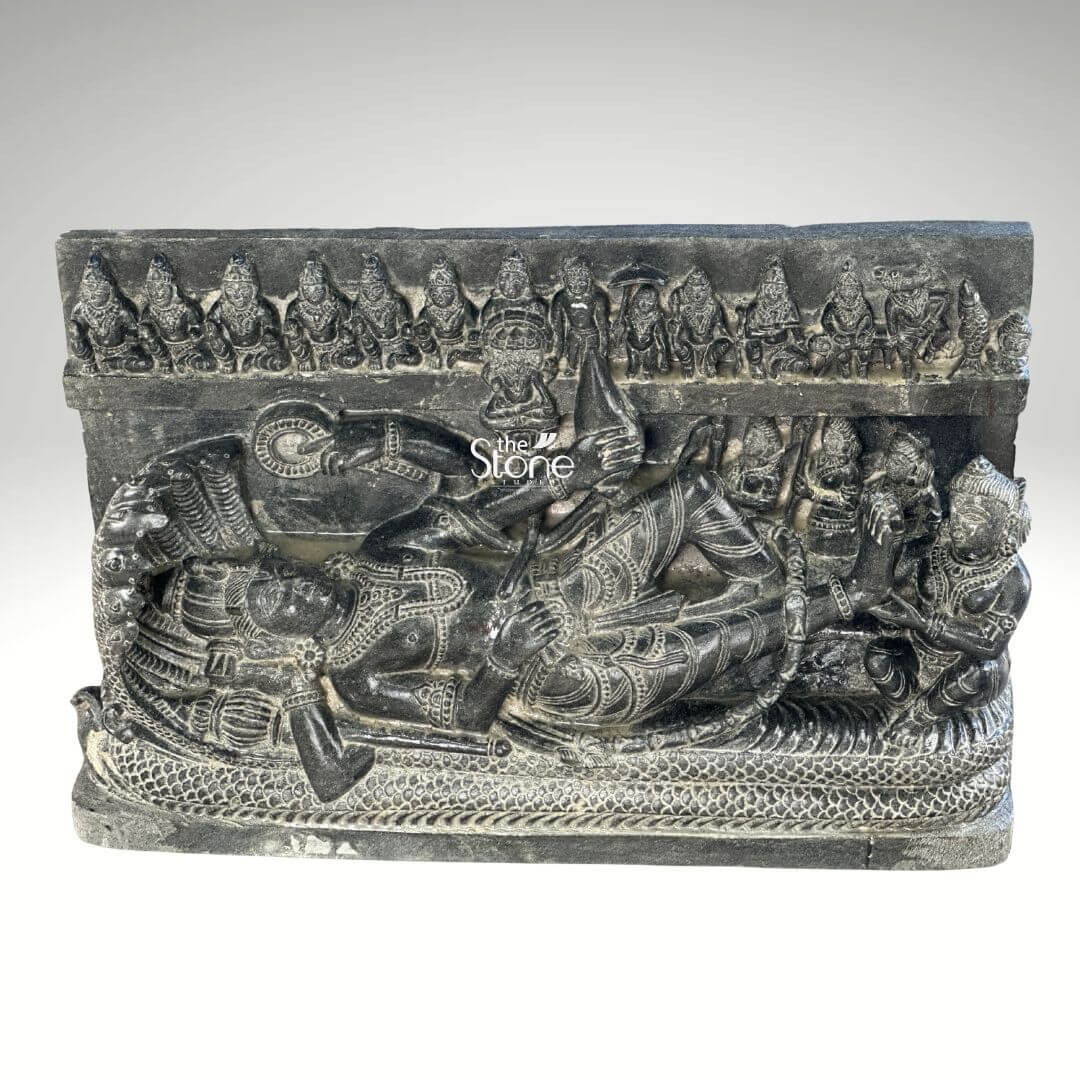 A detailed Ananthasayana Vishnu Stone Statue approximately 30 inches tall depicting the reclining form of Lord Vishnu in his cosmic slumber. The sculpture is carved from a single block of rich blackstone showcasing a deep matte texture that highlights the intricate high-relief carvings. The central figure of Vishnu is shown resting upon the multi-hooded serpent Shesha whose coils form a textured bed beneath him and whose seven hooded heads fan out to create a protective canopy above the deity's crowned head. Vishnu is adorned in traditional regalia including a kiritamukuta elaborate necklaces armlets waistbands and flowing lower garments all rendered with fine detail in the stone. His right hand gently supports his head while his left hand rests along his body holding a conch. The sculpture includes several attendant figures carved in relief. Seated at Vishnu's feet is his consort Goddess Lakshmi who is shown massaging his foot with devotion. Above the main reclining figure a frieze of miniature figures representing the ten avataras of Vishnu is carved horizontally adding a comprehensive narrative to the divine iconography. The entire stele is carved from a deep, rich black stone exhibiting a matte tactile finish that emphasizes the high relief and detailed craftsmanship. The natural variations in the stone's color and texture convey a sense of age and authenticity, consistent with a traditional piece. The sculpture is presented against a plain neutral grey background which isolates the form and draws the viewer's eye directly to the complex narrative and divine iconography depicted in the stone. This detailed carving serves as an exemplary illustration for an article on Ananthasayana Vishnu stone statues.