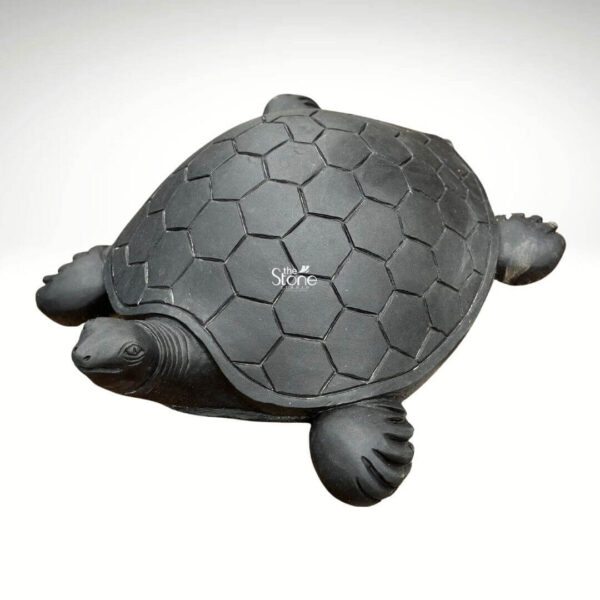A detailed three-quarter view photograph showcasing a magnificent Black Stone Turtle Statue meticulously carved and standing against a clean neutral background. This Blackstone Tortoise statue is expertly hand-carved from a single block of deep dark black stone exhibiting a smooth matte finish that accentuates the natural rich color and texture of the basalt. The turtle is depicted in a realistic walking posture with its head extended forward and its limbs positioned for movement. The carving captures the intricate details of the creature's anatomy with exceptional precision. The carapace is adorned with a beautifully defined symmetrical pattern of hexagonal scutes deeply incised to create a lifelike texture. The head features finely carved eyes a subtle beak and skin folds while the legs and tail display realistic scale patterns showcasing the artisan's skill in traditional Indian stone carving. The overall form is robust and well-proportioned conveying a sense of ancient strength and tranquility associated with the tortoise in Hindu mythology and Vastu. The dark solemn presence of the stone makes this statue a commanding focal point. The photograph captures the perfect symmetry and rich craftsmanship of the masterwork making it a quintessential example of a Black Stone Turtle Statue suitable for spiritual spaces Vastu corrections or art collections.