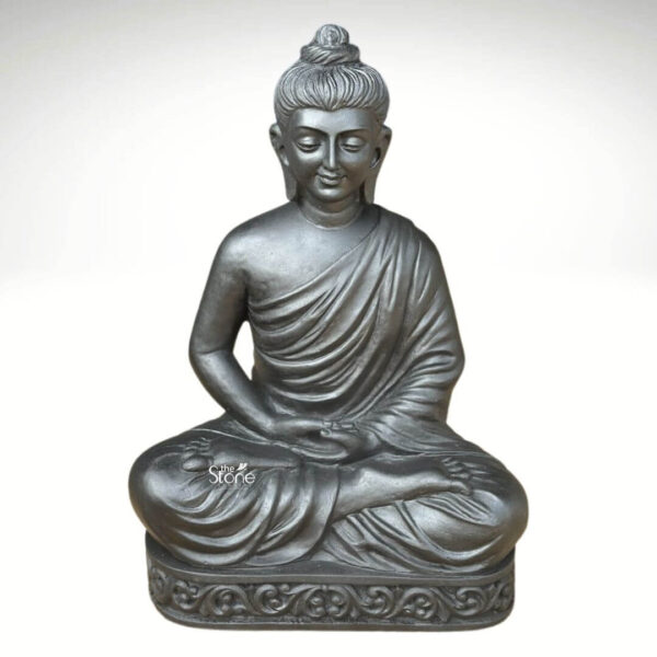 A two-foot-tall meditating Buddha stone statue stands as the central focus presented in a classic three-quarter view against a simple light grey gradient background. The statue is meticulously hand-carved from a single block of deep black stone showcasing a rich polished texture that gleams subtly under the light and conveys a profound sense of sanctity. Lord Buddha is depicted in a traditional seated posture with his legs crossed in a yogic pose and his hands resting gently in his lap in the dhyana mudra or meditation gesture with palms facing upward and thumbs touching. The statue captures a serene and benevolent facial expression with eyes gently closed in contemplation a composed compassionate smile and a peaceful demeanor. His head is adorned with traditional tightly curled ushnisha hair and elongated earlobes both meticulously carved. The flowing folds of the monastic robe are rendered with delicate precision draping gracefully over his left shoulder and across his body adding a sense of movement and realism to the dark stone. The entire figure is seated upon a carved rectangular pedestal which is also adorned with a detailed repeating pattern of stylized leaves and decorative motifs providing a stable and ornate base. This exquisite two-foot blackstone meditating Buddha statue is a perfect embodiment of peace and tranquility expertly crafted to serve as a revered murti for worship or a significant spiritual artifact within a home shrine. The high-quality blackstone material ensures the sculpture's durability and timeless beauty making it a lasting addition to any sacred space. The profound detail in the carving from the serene expression to the delicate folds of the robe and the ornate pedestal showcases the skill of the artisans. The compact two-foot size makes it an ideal choice for placement on a personal altar or pedestal bringing the divine energy of the Buddha into the daily lives of the faithful.