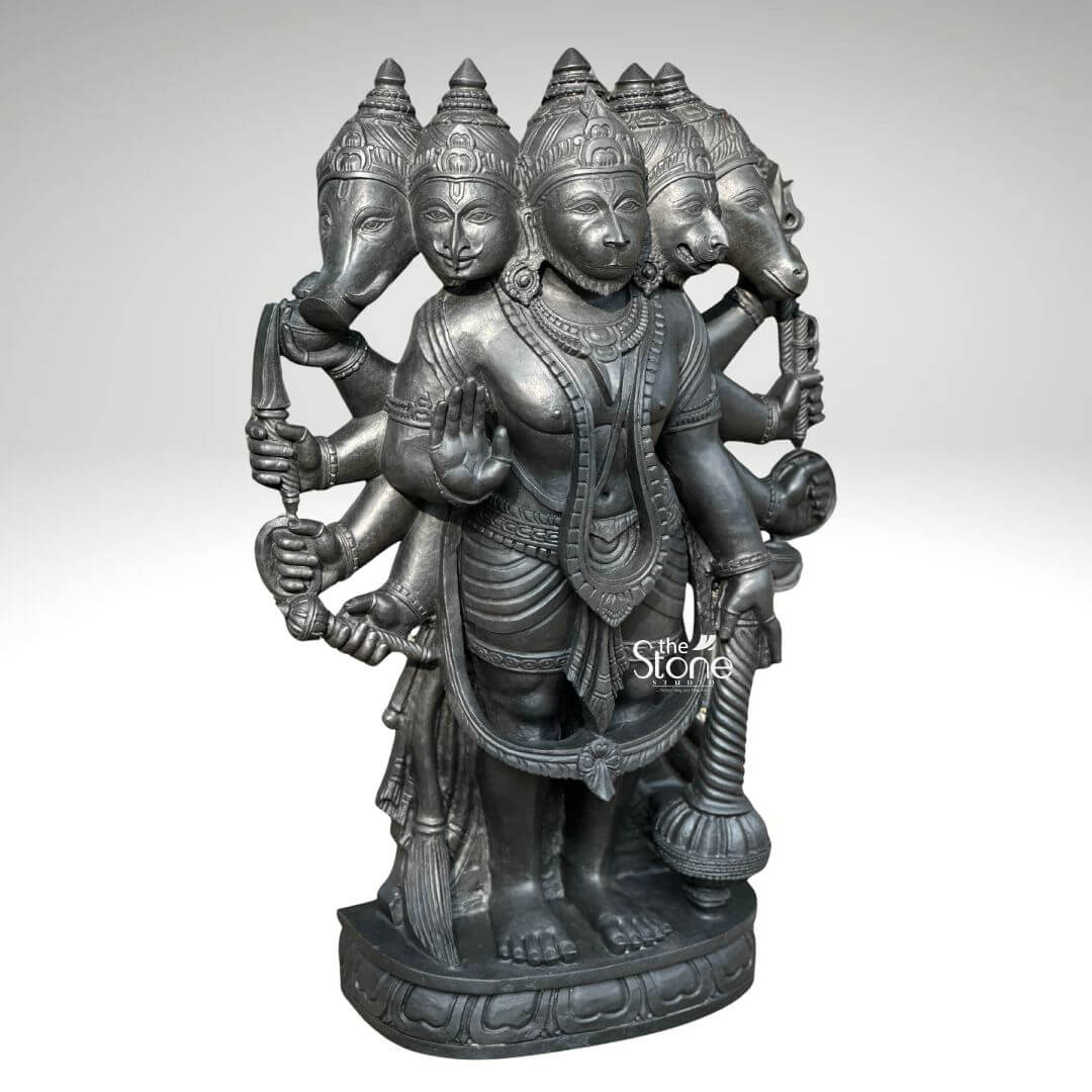 A full-view studio photograph set against a plain light grey background displays a magnificent 3.5-foot Panchamukhi Hanuman Murti for Temple. This intricately hand-carved statue is made from a single block of deep dark blackstone renowned for its durability and fine grain. The murti depicts the five-faced form of Lord Hanuman known as Panchamukhi Hanuman standing firmly on a multi-tiered ornate circular base that is ready for temple installation. The central face is that of Hanuman himself looking forward with a serene protective expression adorned with traditional jewelry and a crown. Radiating outwards from the central head are four other divine faces: to the east the boar face to the south the lion face to the west the eagle face and to the north the horse face. The statue is multi-armed totaling ten arms that hold various divine attributes each rendered with exquisite detail. The main central right hand is raised in the Abhaya mudra while the main central left hand holds a mace that rests on the base. The other eight hands hold a conch discus sword shield noose hook a mountain and a vessel. The deity is adorned with elaborate traditional South Indian carvings of necklaces armlets wristlets a sacred thread and a detailed dhoti all chiseled with precision into the dark stone. The fine texture of the blackstone enhances the depth and shadow of the carvings highlighting the complex iconography of this formidable yet benevolent form of Hanuman. This Panchamukhi Hanuman Murti is specifically designed for temple sanctum placement embodying the combined power of the five deities represented by the faces. The 3.5-foot height makes it a commanding presence suitable for daily puja and darshan within a large temple hall. The blackstone material gives the statue a timeless ancient feel ensuring it will be a revered centerpiece for generations of devotees. The statue's detailed iconography from the expressions on the five faces to the specific items held in the ten hands makes it a significant subject for study and devotion. The expert craftsmanship transforms the raw stone into a vibrant sacred form fulfilling the requirements for a traditional temple vigraham.