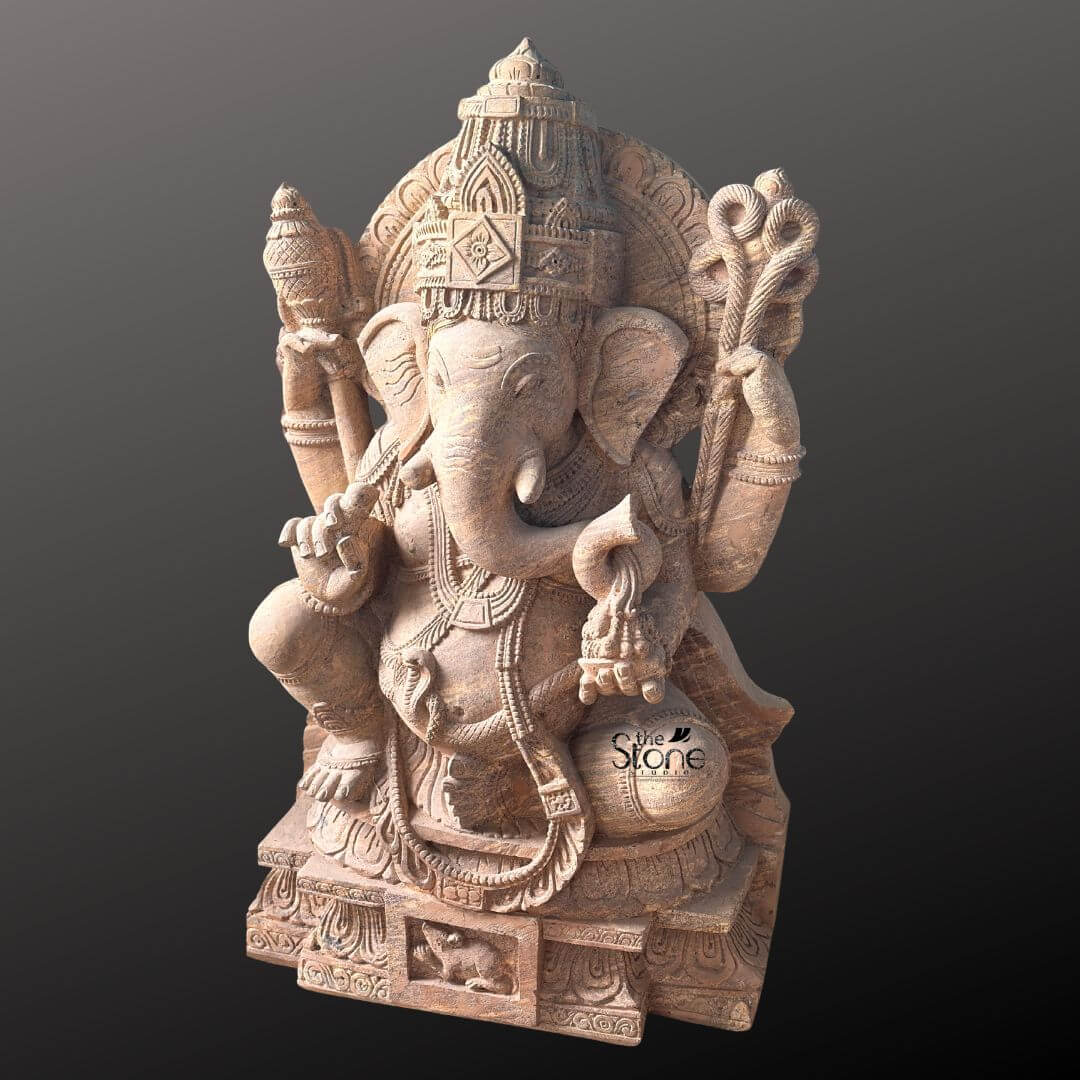 A detailed three-quarter view photograph of a magnificent Vinayagar Stone Statue meticulously hand-carved from a single block of warm beige sandstone. The statue stands approximately four feet tall and is depicted in a traditional seated posture known as lalitasana with one leg gracefully folded and the other slightly pendant resting upon a decorated base. The four-armed deity is seated upon an intricately carved multi-tiered lotus pedestal which is further embellished with detailed floral and geometric patterns and features a small finely carved figure of Ganesha's vehicle the mouse centrally at its base. The sandstone exhibits a natural warm texture typical of the material showcasing the artisan's skill in achieving fine detail in the deity's form and ornaments. Vinayagar or Lord Ganesha is richly adorned with abundant deeply carved traditional jewelry and ornaments all rendered in the same sandstone. He wears a detailed jeweled mukuta featuring a prominent central gem and peacock motifs multiple necklaces of varying lengths elaborate armlets wristlets and anklets. His sacred thread is intricately carved across his torso. The deity holds symbolic attributes in his four hands: his upper right hand holds an axe and his upper left hand holds a noose while his lower right hand is raised in a gesture of blessing and his lower left hand holds a sweet towards his trunk. The trunk itself curves elegantly to the left holding the modak. This commanding 4 feet statue embodies the spiritual essence and iconographic details of the remover of obstacles making it a suitable and sacred focal point for a home shrine or temple sanctum. The face of Vinayagar is serene and benevolent with downcast eyes conveying deep wisdom and compassion. The careful carving of every element from the tassels of his garments to the petals of the lotus throne reflects centuries-old sculpting traditions. The overall composition is balanced and reverent highlighting the divine form of Lord Ganesha. The photograph captures the statue against a plain dark grey studio background emphasizing the detailed craftsmanship and the natural beauty of the sandstone.