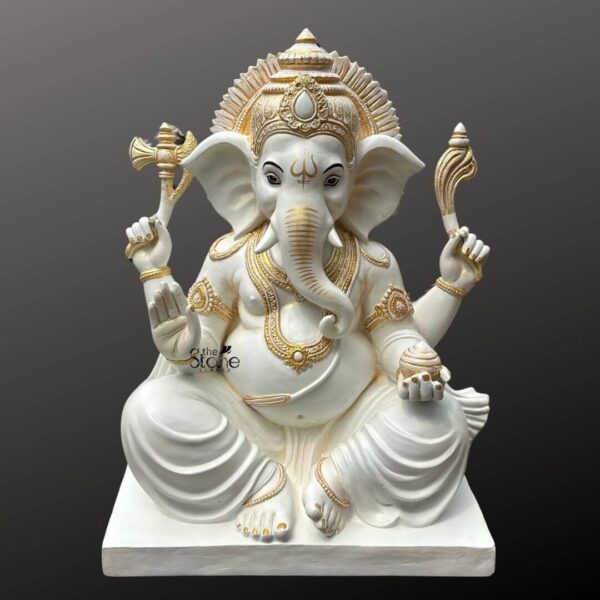 A three-foot-tall fibre statue of the Hindu deity Vinayaka Ganapathi, also revered as Ganesha, is presented against a clean, dark grey gradient studio background, showcasing the sculpture in its entirety. The statue is finished in a pristine matte white, which serves as a canvas for opulent, raised gold leaf accents that meticulously highlight its form and ornaments. Ganesha is depicted in a traditional seated posture, with his right leg folded and left leg slightly raised, resting on a simple, integrated white fibre pedestal. The artisan has applied intricate gold detailing to his elaborate crown (mukut), large fan-like ears, eyes with defined pupils, multiple necklaces (mala), armbands (vanki), bracelets (kangan), waist belt (udara bandha), anklets, and the delicate folds of his flowing dhoti. His right upper hand holds a golden ankusha (goad) and his left upper hand holds a golden pasha (noose), both richly detailed. His lower right hand is in the Abhaya Mudra, bestowing blessings, while his lower left hand holds a modak (sweet) resting in his lap. The entire statue exhibits fine craftsmanship, with the lightweight yet durable fibreglass material allowing for precise sculpting of the divine features and decorative elements. The matte white and burnished gold color scheme gives the statue a contemporary yet traditional aesthetic, making it a versatile option for various home decor settings. The clean, focused lighting emphasizes the three-dimensional quality of the sculpture and the reflective nature of the gold leaf work. This image effectively illustrates the beauty and craftsmanship of a Vinayaka Ganapathi fibre statue, making it an excellent visual reference for the article. The three-foot height strikes a perfect balance between being a commanding presence and fitting into diverse home spaces, from a dedicated puja room to a living area. The detailed carving and luxurious gold accents highlight the high quality achievable with fibreglass, offering a durable and aesthetically pleasing alternative to traditional stone or metal idols. The neutral background ensures the focus remains entirely on the deity, allowing the viewer to appreciate the intricate details and the serene expression on Ganesha’s face.