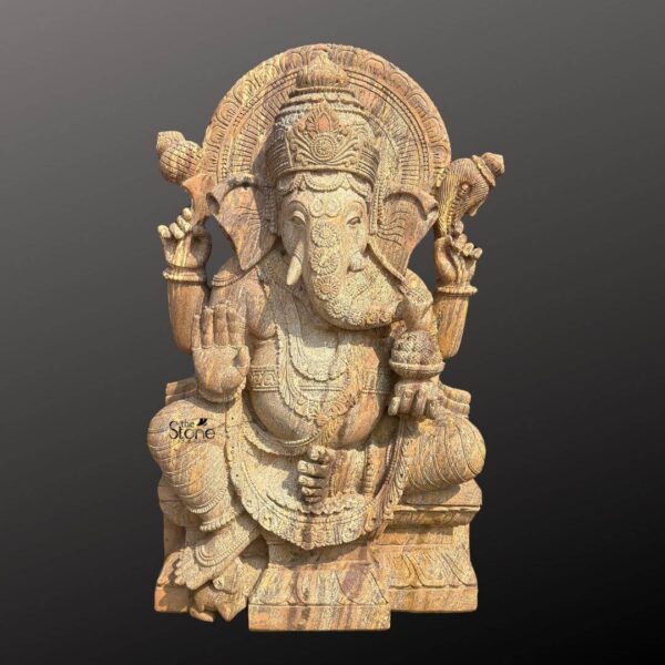 A magnificent four-foot-tall Vinayaka Ganapathi stone statue stands as a testament to traditional Indian craftsmanship. Carved from a warm textured sandstone the statue depicts the Hindu deity Ganesha in a traditional seated posture known as the Lalitasana pose with his right leg folded and left leg slightly raised. The natural variations and grain of the stone are visible across the sculpture giving it an earthy ancient feel that is well-suited for a consecrated space. The artisan has lavished attention on the intricate details from the ornate crown and elaborate jewelry adorning his form to the delicate folds of his flowing dhoti. Ganesha is depicted with four arms each holding a symbolic item his upper right hand holds an ankusha his upper left holds a pasha and his lower right hand is in the Abhaya Mudra bestowing blessings. His lower left hand holds a modak resting in his lap. The statue features a prominent finely carved prabhavali behind the deity adorned with traditional patterns and culminating in a kirtimukha at the apex. He is seated on a robust lotus-petal-carved pedestal providing a stable and grand base for the entire sculpture. This four-foot Vinayaka Ganapathi stone statue is an ideal size for a prominent home shrine a temple entrance or a garden sanctuary. The substantial weight and durable sandstone material ensure its longevity making it a lasting investment for spiritual practice or decor. The natural daylight photograph against a dark grey gradient background emphasizes the statue's three-dimensional quality and the artisan's meticulous work on the serene facial expression and decorative elements. This piece perfectly illustrates the divine grace and cultural richness that a well-crafted stone Ganesha statue brings to any environment.