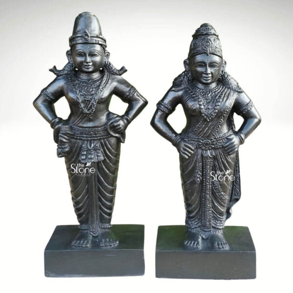 A full eye-level photograph capturing a pair of intricately hand-carved Vithoba and Rakhumai Black Stone Statues standing side-by-side on individual square black stone bases. The statues measuring approximately 15 inches in height are crafted from a single block of dark polished black stone showcasing the deep uniform color and subtle natural variations inherent to the material. Both deities are depicted in their traditional standing posture facing forward with composed benevolent expressions embodying the classical South Indian sculpting style. Lord Vithoba on the left stands with his arms akimbo holding a conch shell in his upper right hand and a discus in his upper left hand while his lower hands rest on his hips. He is adorned with elaborate finely detailed traditional jewelry including multiple necklaces armlets wristlets anklets a sacred thread and a tall cylindrical mukuta. His dhoti is intricately carved with decorative patterns and folds accented with a prominent pitambar and various ornaments. His feet are adorned with carved sandals and a small decorative cloth hangs over his right arm. Goddess Rakhumai on the right stands parallel to Vithoba also with her arms akimbo in a graceful posture. She is depicted wearing a richly detailed traditional saree featuring ornate patterns borders and folds that flow elegantly around her form. She is adorned with abundant finely carved traditional jewelry, including multiple necklaces elaborate armlets wristlets anklets and a decorative mukuta upon her head. Her hair is tied in a traditional style and a floral garland is carved around her neck. Her hands are adorned with carved bangles and a decorative sash hangs over her left shoulder. This pair of 15 inch Vithoba Rakhumai Black Stone Statues serves as a beautiful and spiritual representation of the divine couple suitable for worship or as a significant decorative art piece. The deep black stone provides a sense of permanence and divinity while the exceptional craftsmanship highlights every detail of their form and ornamentation. The overall composition conveys a profound sense of devotion and artistry consistent with the traditions of Indian temple sculpture. The careful attention to detail from the facial features to the textures of the jewelry and garments reflects centuries-old sculpting techniques. The statues stand on polished black stone pedestals and are presented against a plain light grey studio background.A full eye-level photograph capturing a pair of intricately hand-carved Vithoba and Rakhumai Black Stone Statues standing side-by-side on individual square black stone bases. The statues measuring approximately 15 inches in height are crafted from a single block of dark polished black stone showcasing the deep uniform color and subtle natural variations inherent to the material. Both deities are depicted in their traditional standing posture facing forward with composed benevolent expressions embodying the classical South Indian sculpting style. Lord Vithoba on the left stands with his arms akimbo holding a conch shell in his upper right hand and a discus in his upper left hand while his lower hands rest on his hips. He is adorned with elaborate finely detailed traditional jewelry including multiple necklaces armlets wristlets anklets a sacred thread and a tall cylindrical mukuta. His dhoti is intricately carved with decorative patterns and folds accented with a prominent pitambar and various ornaments. His feet are adorned with carved sandals and a small decorative cloth hangs over his right arm. Goddess Rakhumai on the right stands parallel to Vithoba also with her arms akimbo in a graceful posture. She is depicted wearing a richly detailed traditional saree featuring ornate patterns borders and folds that flow elegantly around her form. She is adorned with abundant finely carved traditional jewelry, including multiple necklaces elaborate armlets wristlets anklets and a decorative mukuta upon her head. Her hair is tied in a traditional style and a floral garland is carved around her neck. Her hands are adorned with carved bangles and a decorative sash hangs over her left shoulder. This pair of 15 inch Vithoba Rakhumai Black Stone Statues serves as a beautiful and spiritual representation of the divine couple suitable for worship or as a significant decorative art piece. The deep black stone provides a sense of permanence and divinity while the exceptional craftsmanship highlights every detail of their form and ornamentation. The overall composition conveys a profound sense of devotion and artistry consistent with the traditions of Indian temple sculpture. The careful attention to detail from the facial features to the textures of the jewelry and garments reflects centuries-old sculpting techniques. The statues stand on polished black stone pedestals and are presented against a plain light grey studio background.